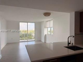 Kitchen featuring a stone-composite countertop, undermount sink, and high-arc faucet, with wood-finish flooring and sliding glass doors leading to a balcony