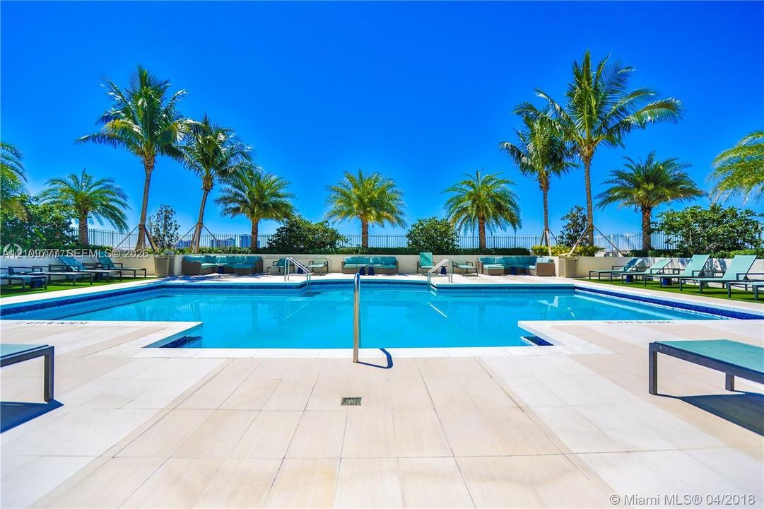 Swimming pool with tile surround, metal handrail, and perimeter landscaping featuring mature palm trees
