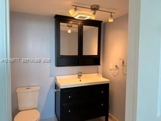 Dark-finish vanity with an integrated white sink and basin, matching mirrored wall cabinet, and multi-light track fixture