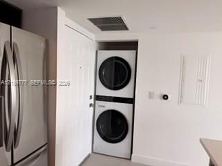 Stacked white front-load washer and dryer unit, stainless steel French door refrigerator, and flush-mounted wall circuitry panel