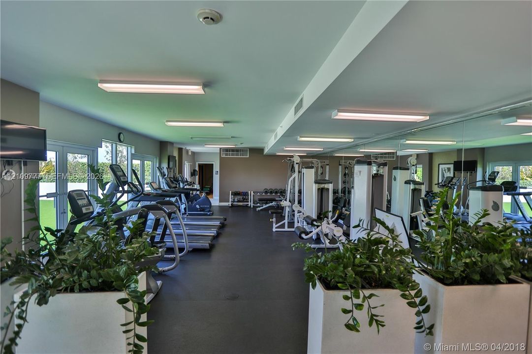 Fitness center featuring full-length wall mirrors, high-impact rubberized flooring, and glass-paneled double doors providing natural light