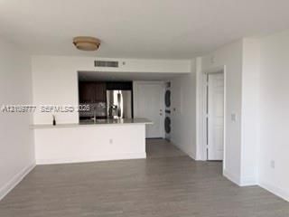 Open-concept kitchen featuring dark wood cabinetry, stainless steel appliances, a stone-surface breakfast bar, and wood-finish flooring