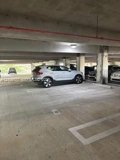 Covered parking area featuring concrete flooring, structural columns, and overhead lighting