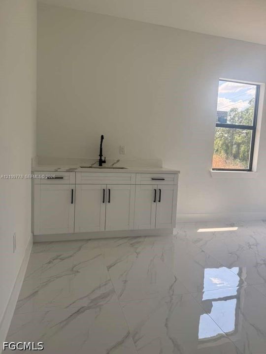 Wet bar featuring white cabinetry, a solid-surface countertop with an integrated sink, and a matte black faucet, complemented by polished stone-finish floor tile