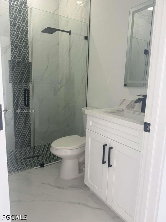 Bathroom featuring a white vanity with matte black hardware, a walk-in shower with glass enclosure, oversized wall and floor tiles, mosaic tile shower accents, and a rainfall showerhead