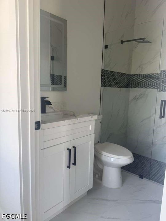 White cabinetry with black hardware, stone-finish countertop, rectangular sink, walk-in shower with glass enclosure, and patterned tile accents