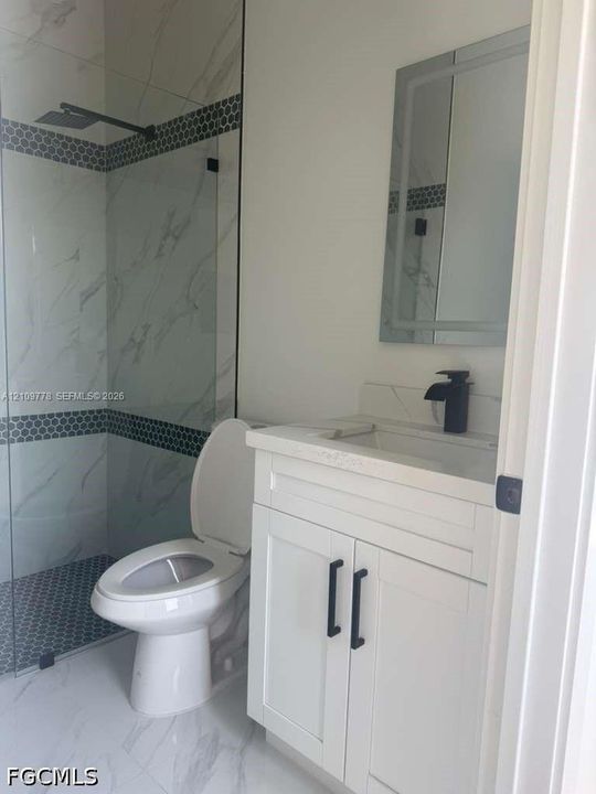 Bathroom featuring a glass-enclosed shower with tiled walls and decorative border, vanity with stone-composite countertop, matte black faucet, and frameless illuminated mirror