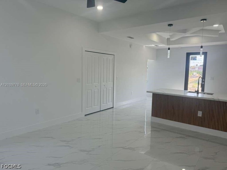 Interior space featuring polished porcelain tile flooring, tray ceiling with recessed lighting, kitchen island with slatted wood detailing and stone-finish countertop, dual pendant lights, and double-panel closet doors