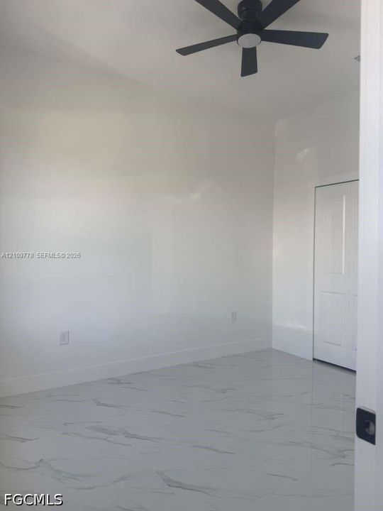 Interior space featuring large-format tile flooring with a neutral veined pattern, crisp white walls, and a matte black ceiling fan