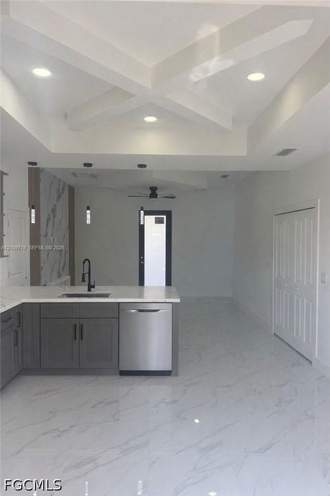 Coffered ceiling with recessed lighting, large-format tile flooring, gray cabinetry with stone-finish countertops, stainless steel dishwasher, and matte black plumbing fixtures