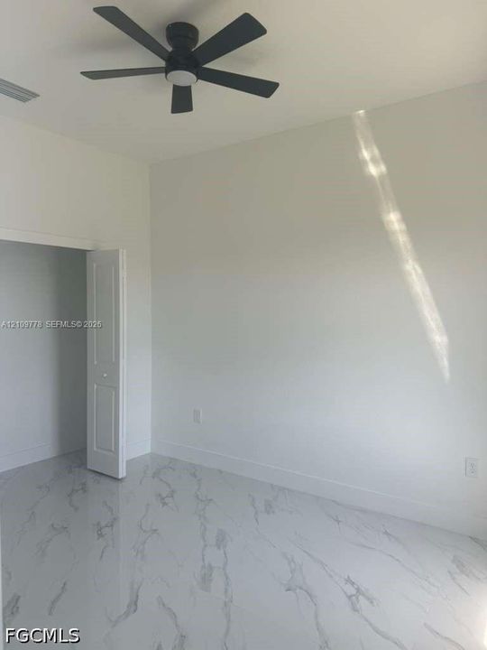 High-ceilinged room featuring large-format stone-finish tile flooring, matte black ceiling fan with integrated lighting, and a bi-fold door