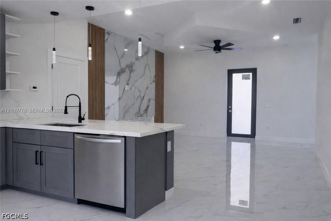 Kitchen featuring a stone-finish island countertop, matte black faucet, stainless steel dishwasher, full-height decorative wall paneling, and polished tile flooring