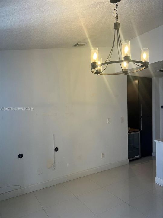 Circular metal chandelier with glass shades, polished tile flooring, and dark-toned built-in cabinetry featuring an integrated beverage refrigerator