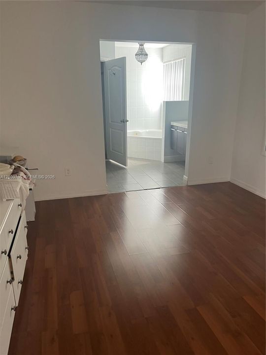 Room featuring wood-finish flooring, tile flooring in the secondary space, a soaking tub, and a hanging pendant light fixture