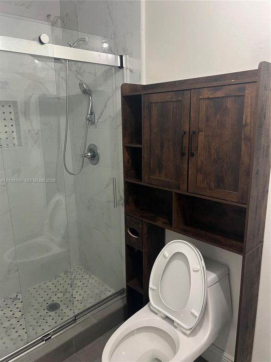 Walk-in shower featuring a frameless glass door, stone-finish wall tile, a built-in recessed niche, and a handheld shower fixture