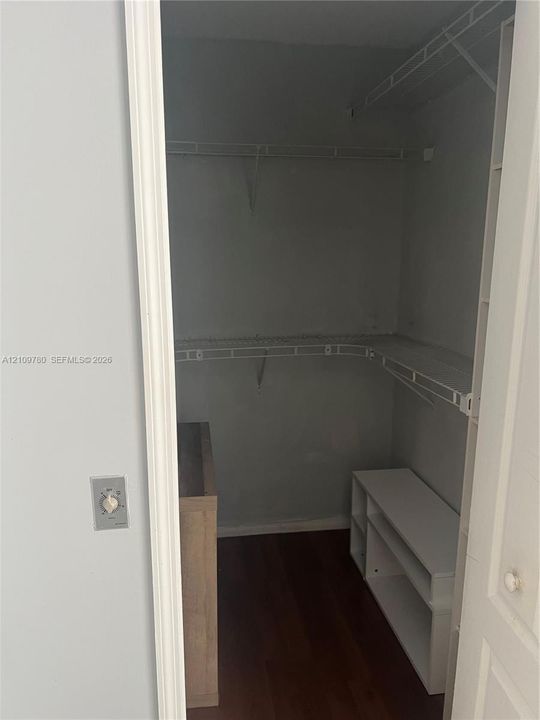Storage space featuring white wire shelving, wood-finish flooring, and built-in white tiered shelving