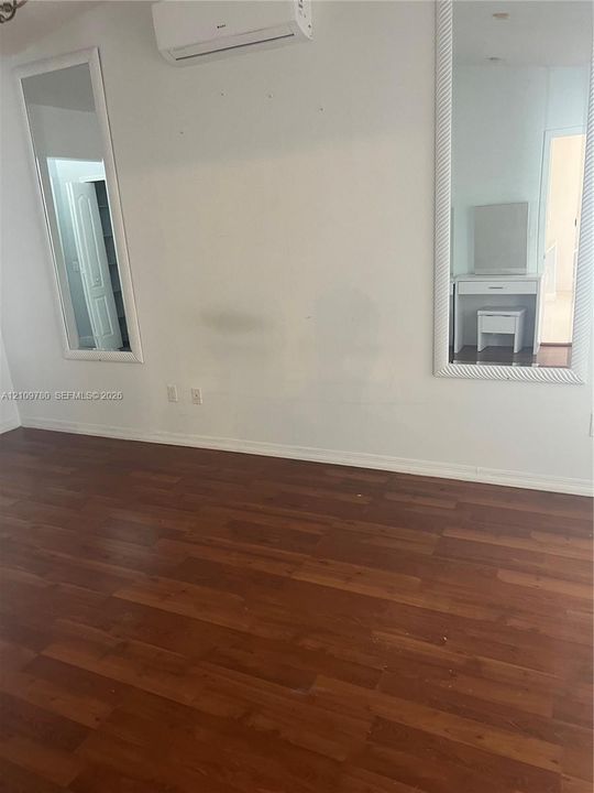 Interior space featuring wood-finish flooring, two large wall-mounted mirrors with white frames, and a wall-mounted ductless climate control unit