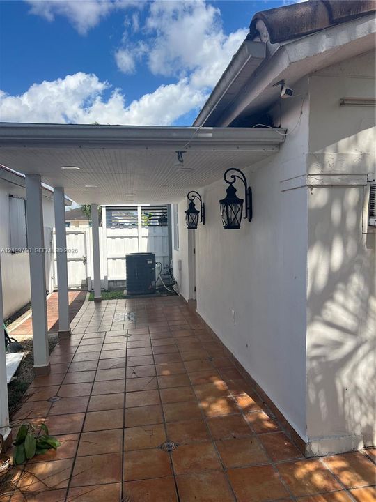 Covered patio featuring ceramic tile flooring, beadboard ceiling, iron-style wall sconces, and structural support columns