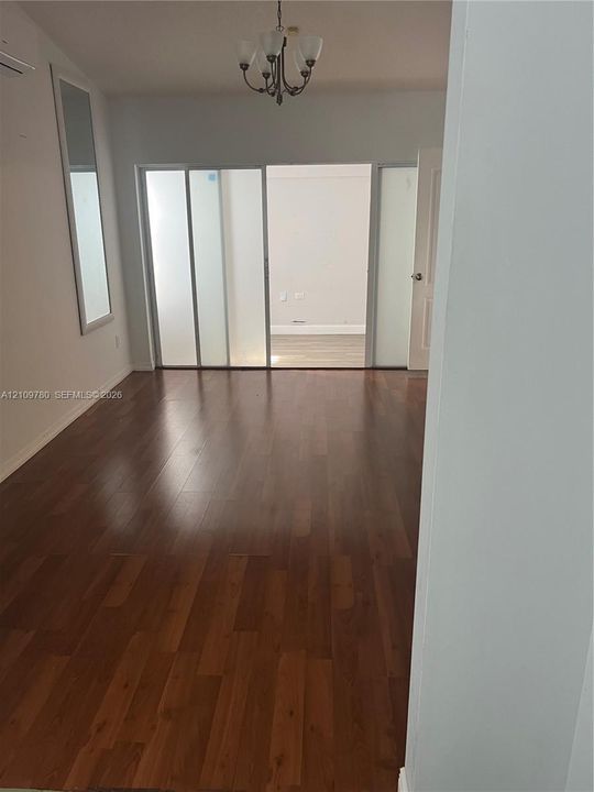 Interior space featuring wood-finish flooring, a five-arm candelabra-style chandelier, and floor-to-ceiling sliding glass room dividers with opaque panels