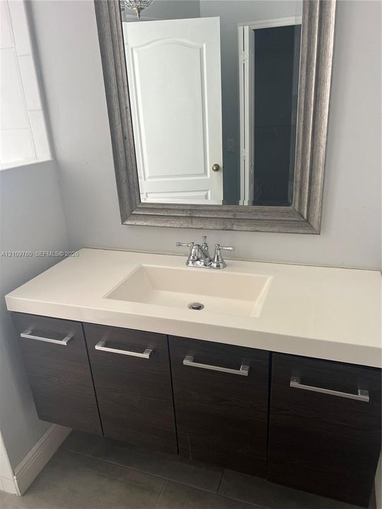Floating vanity featuring a dark wood-finish, integrated sink with a solid surface countertop, chrome hardware, and a framed wall mirror
