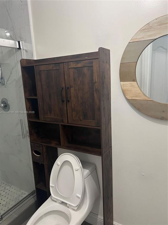 Glass-enclosed shower with large-format tile surround, integrated wood-finish storage cabinetry, and circular wall-mounted mirror