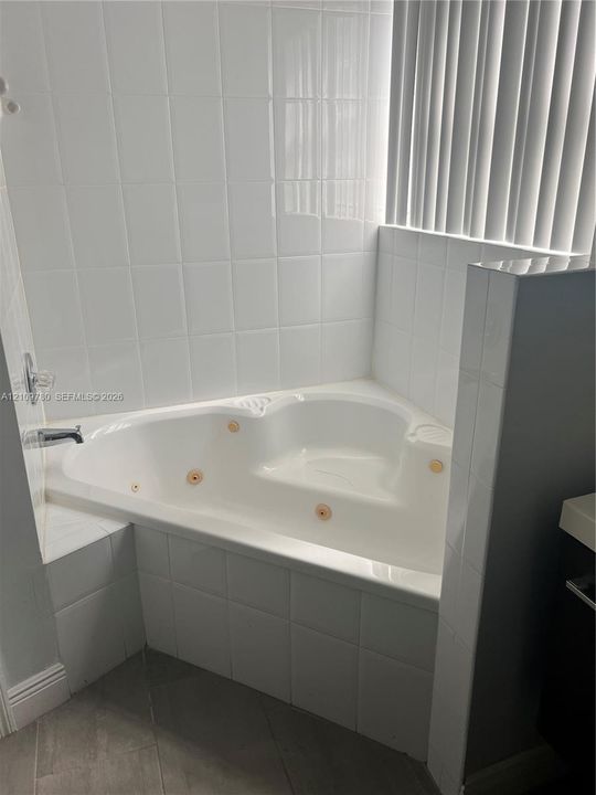 Corner jetted soaking tub featuring white tile surround, chrome fixtures, and built-in molded shelving