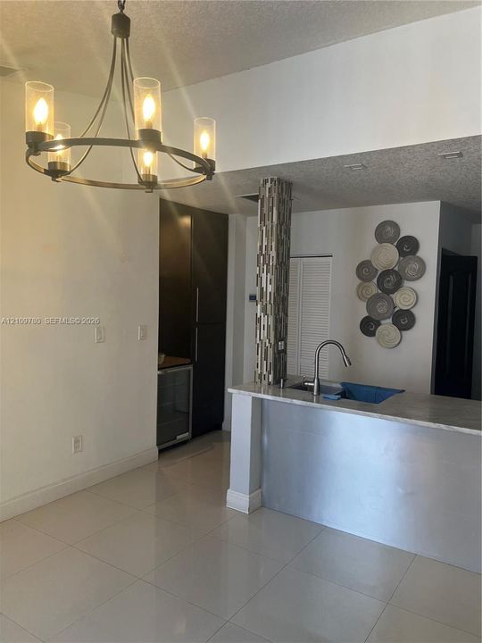 Kitchen area featuring a stone-topped island with an undermount sink and faucet, custom floor-to-ceiling cabinetry, a built-in under-counter beverage cooler, a mosaic-tiled column, and a multi-arm metal chandelier