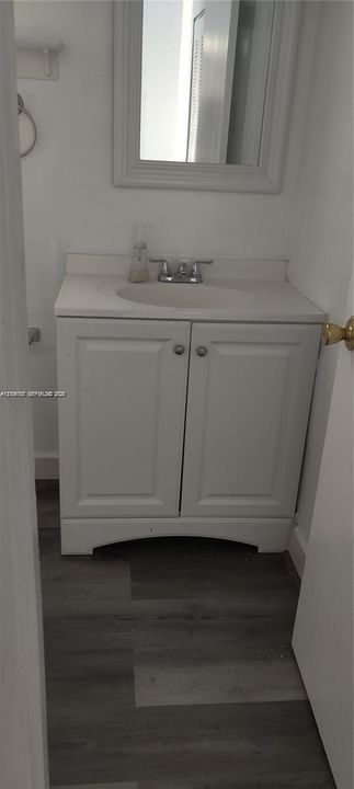 White vanity cabinet featuring an integrated countertop with a drop-in sink, chrome-finish faucet, framed wall mirror, and wood-finish flooring