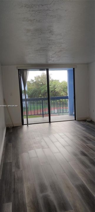 Wood-finish flooring throughout, sliding glass doors, and a covered balcony with a metal railing