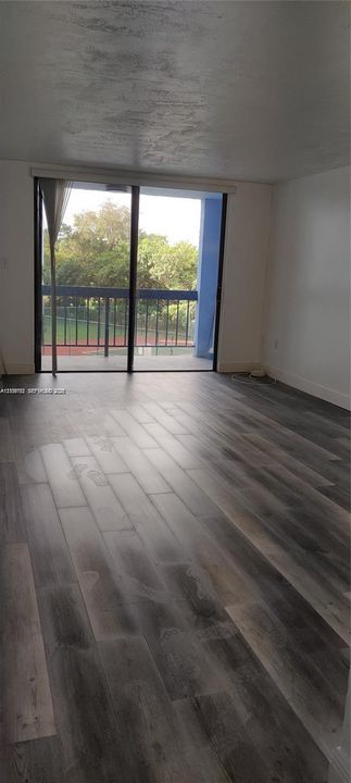 Living area featuring wood-finish flooring and floor-to-ceiling sliding glass doors opening to a private balcony with metal railings