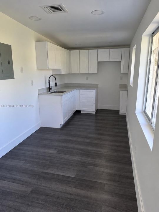 White shaker-style cabinetry, neutral stone-finish countertops, wood-finish flooring, recessed lighting, and a matte black gooseneck faucet