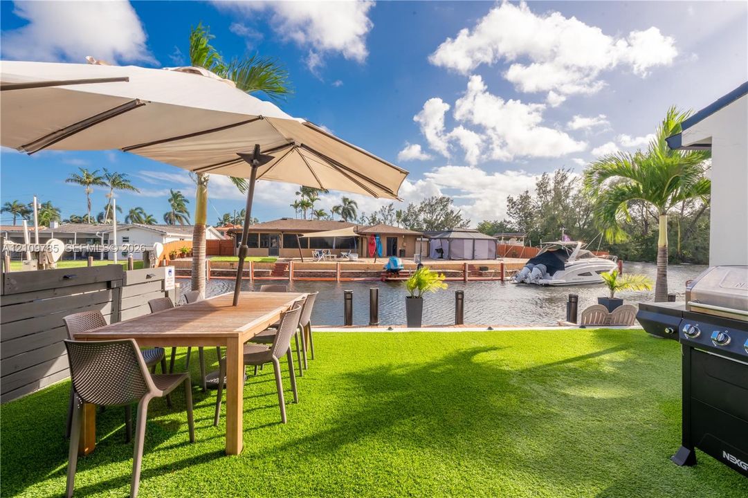 Waterfront patio featuring synthetic turf, wood-tone fencing, and direct canal access with bulkhead docking