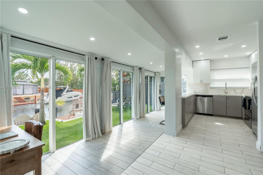 Kitchen featuring stainless steel appliances, white upper cabinetry, grey lower cabinetry, and recessed lighting, paired with floor-to-ceiling glass sliding doors opening to a waterfront lawn and boat dock
