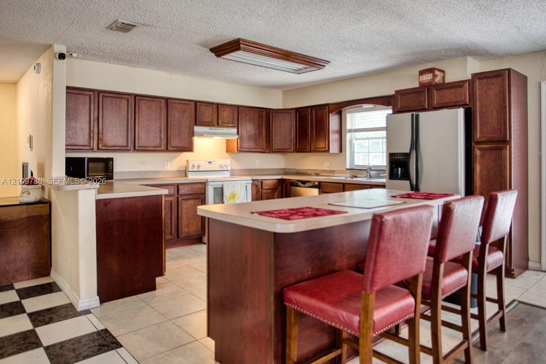 Kitchen featuring warm-toned cabinetry, central island with seating counter, light-colored countertops, and tile flooring