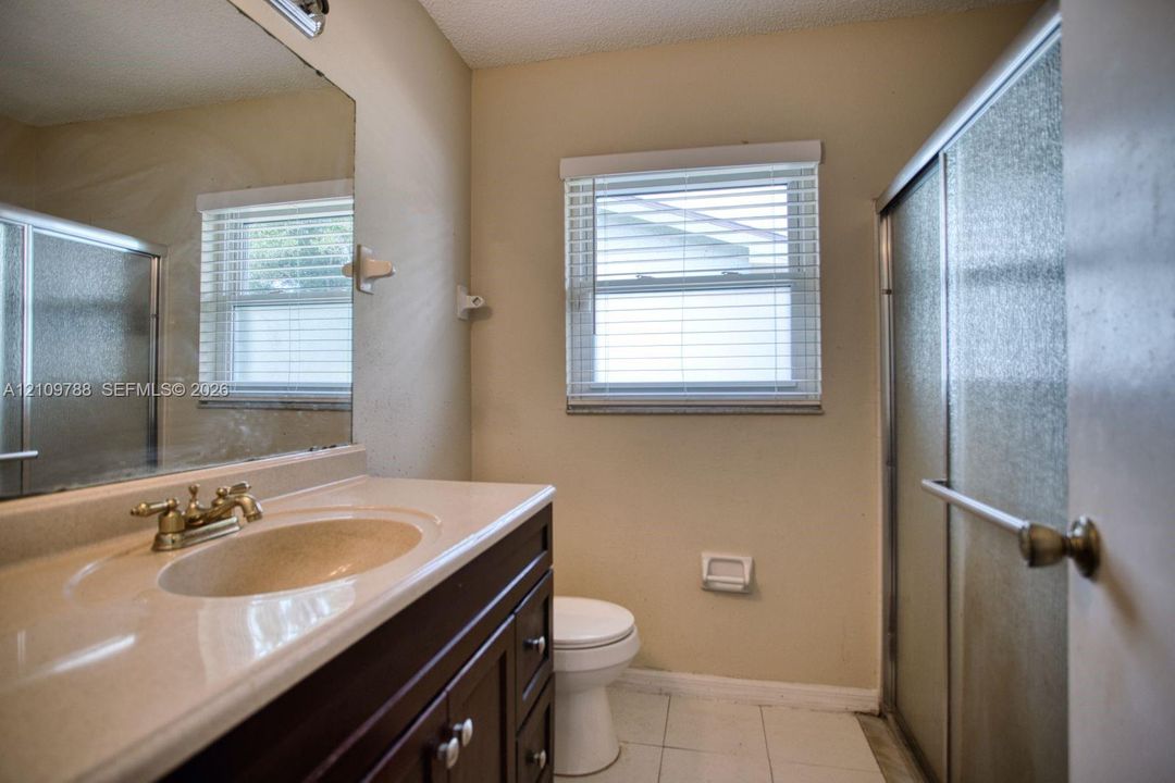 Dark wood-finish vanity with an integrated basin, countertop, polished metal faucet, wall-spanning mirror, and glass-enclosed shower