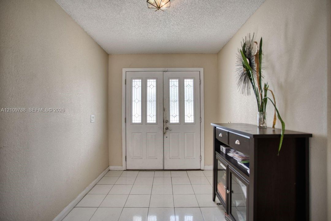 Entryway featuring white double doors with decorative glass inserts, neutral wall finishes, and white ceramic tile flooring under a flush-mount geometric light fixture