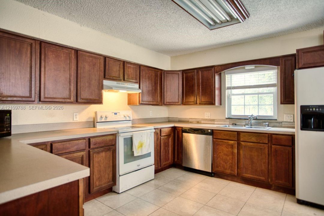 Kitchen featuring stained wood cabinetry, solid surface countertops, tile flooring, stainless steel dishwasher, and a window above the sink