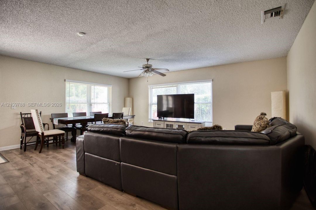 Spacious living area featuring wood-finish flooring, dual windows with natural lighting, and a ceiling fan with integrated light fixture