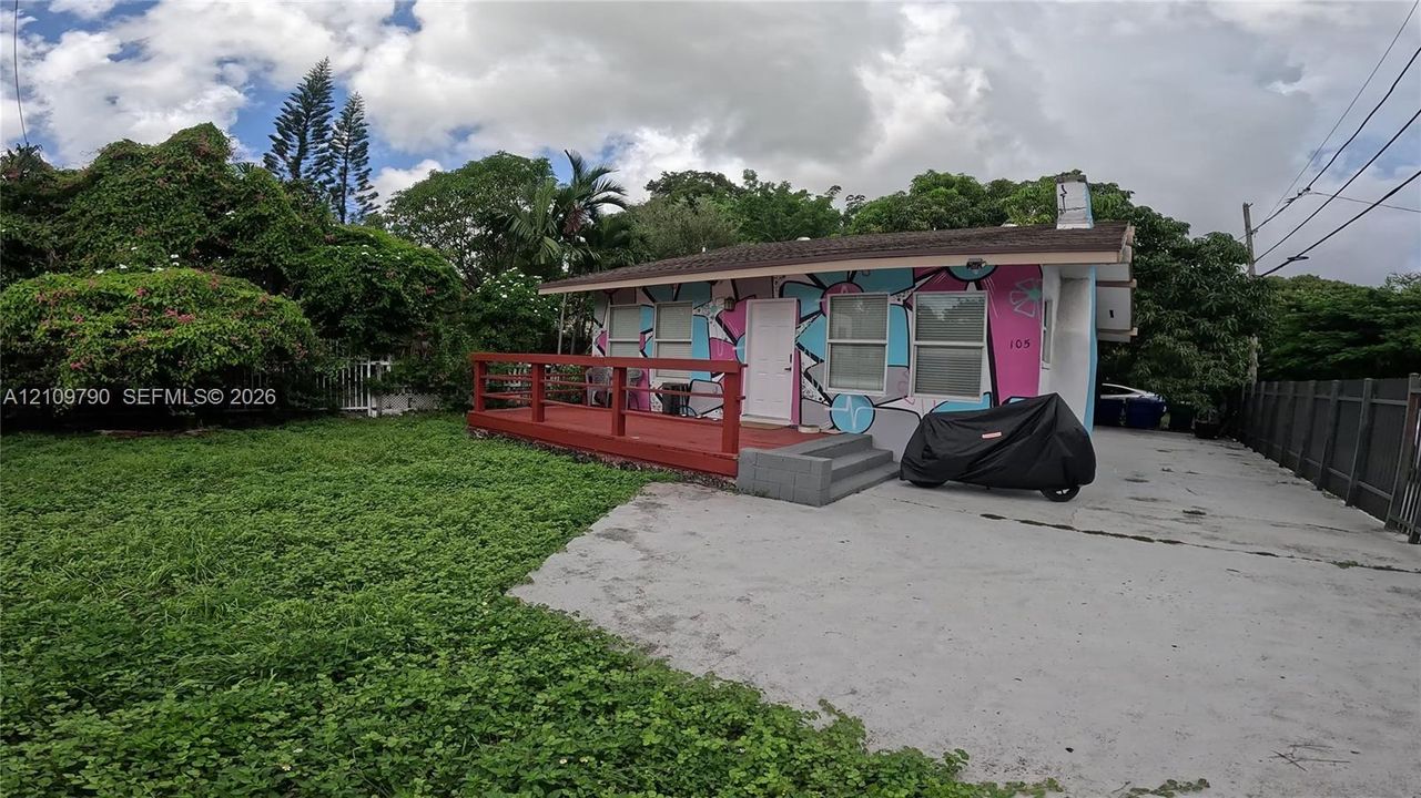 Single-story exterior featuring a red-painted wood deck, concrete driveway, and solid fence perimeter
