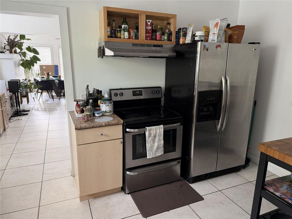 Kitchen area featuring stainless steel side-by-side refrigerator, electric range, stainless steel range hood, natural wood-finish cabinetry, and tiled flooring