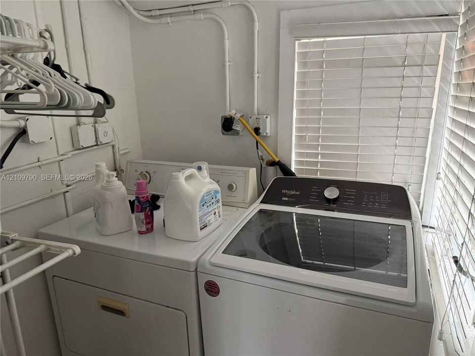 Dedicated laundry area featuring a top-load washer, a built-in dryer, white wall-mounted garment rack, and horizontal slat window blinds