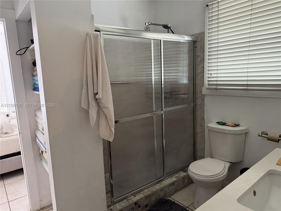 Shower enclosure featuring a chrome-frame sliding door, walk-in design with a tiled threshold, built-in recessed shelving, two-piece toilet, and vanity with an integrated basin
