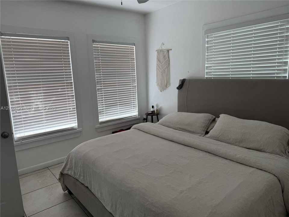 Neutral-toned room featuring light-colored tile flooring, triple windows with horizontal blinds, and a ceiling fan