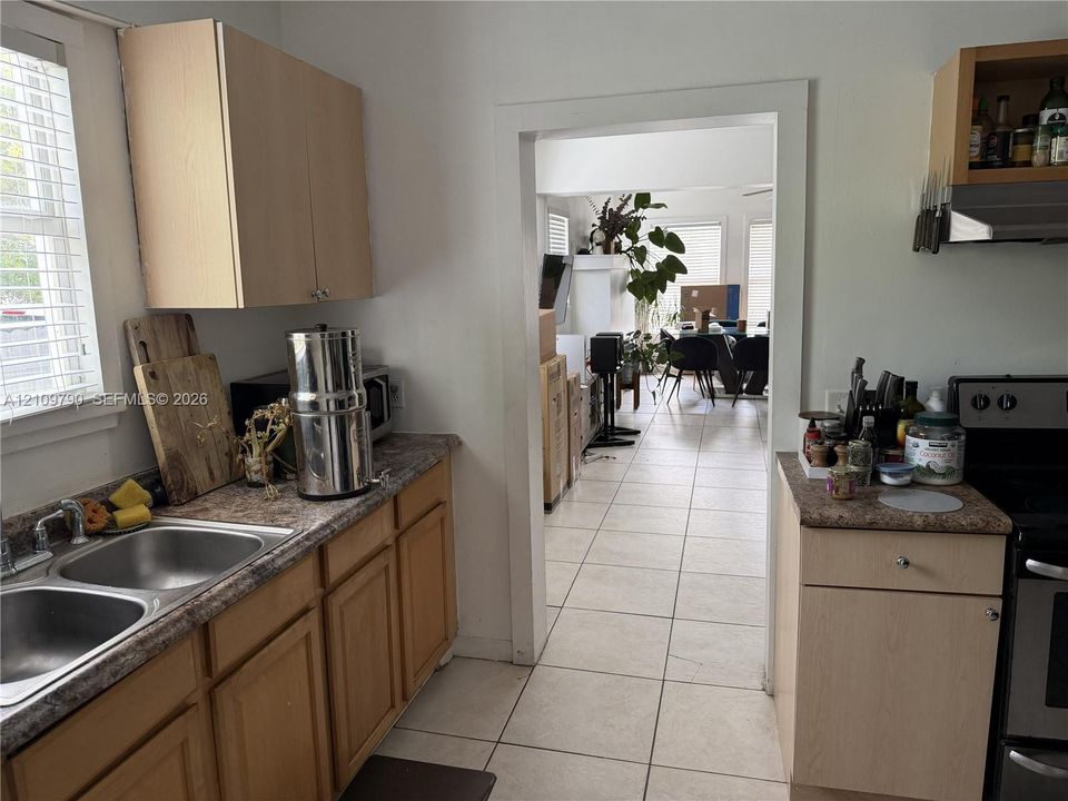 Kitchen featuring light wood-finish cabinetry, laminate countertops, a double-basin stainless steel sink, and ceramic tile flooring
