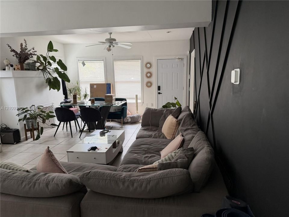 Accent wall featuring geometric molding, large-format tile flooring, ceiling fan, and fireplace surround