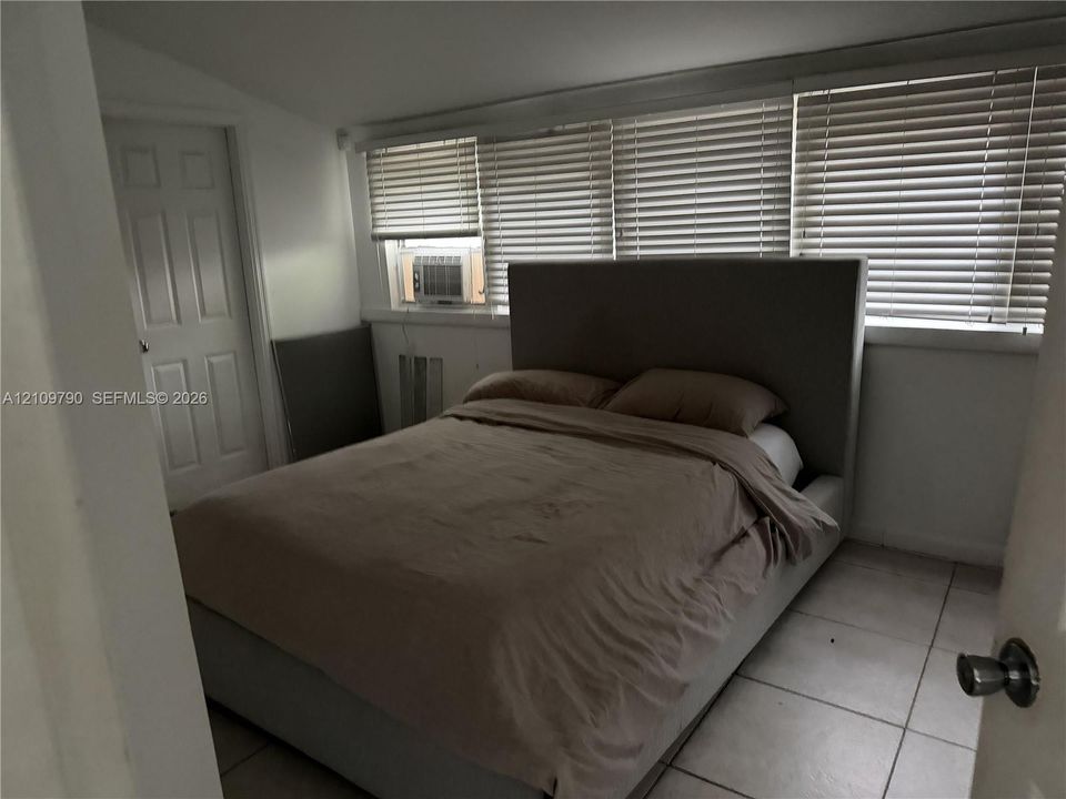 Room featuring neutral tile flooring, a multi-panel door, and a wall of windows fitted with horizontal blinds