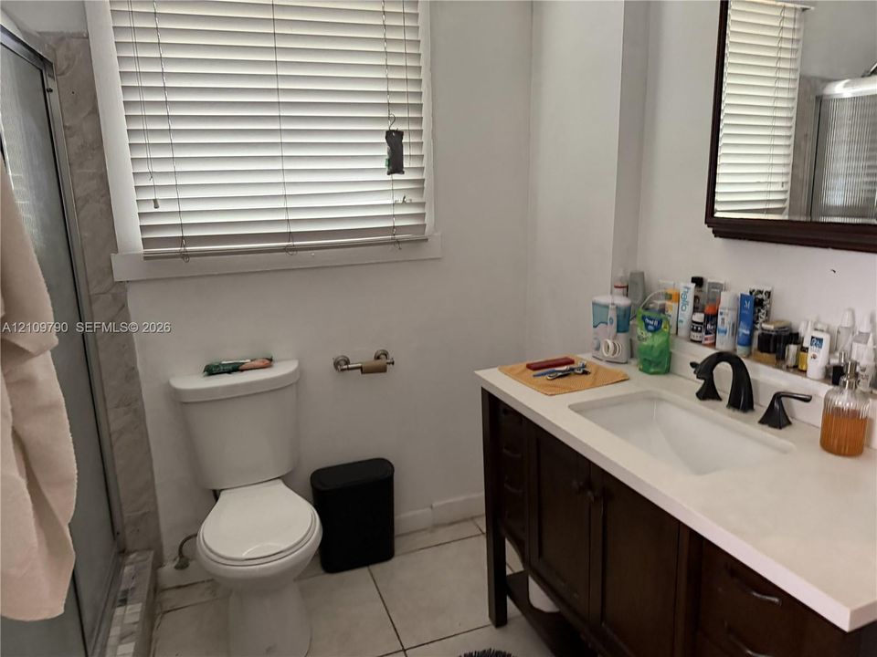 Bathroom featuring a dark wood-finish vanity, light-toned stone countertop, undermount sink with dark metal hardware, ceramic floor tile, and shower enclosure with glass door