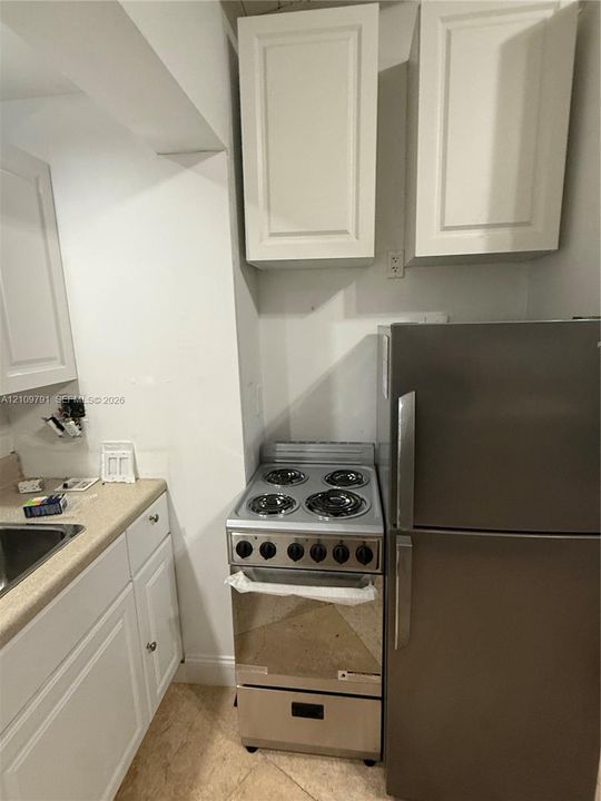 White shaker-style cabinetry, neutral stone-finish countertops, stainless steel electric range, and stainless steel refrigerator