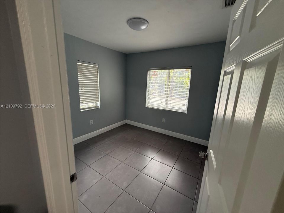 Room featuring large-format ceramic tile flooring, neutral grey wall paint, and two windows equipped with horizontal blinds