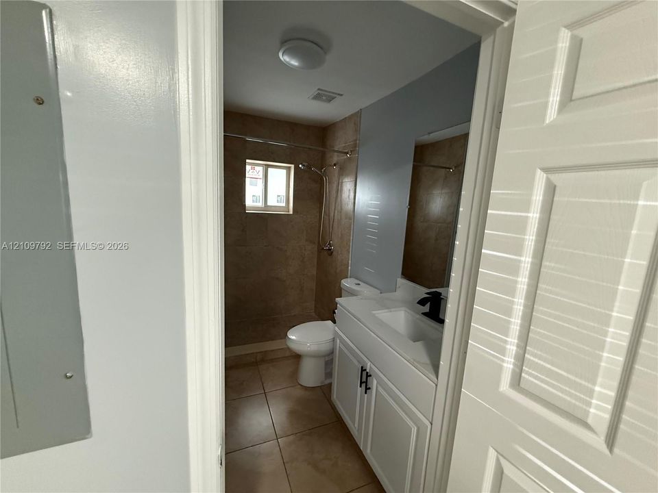 Bathroom featuring a white vanity cabinet with a rectangular vessel sink, matte black faucet, stone-finish floor tiling, and a tiled shower enclosure
